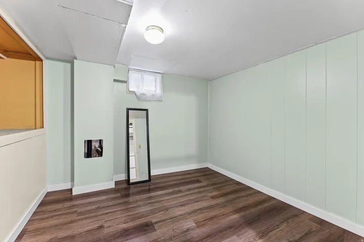 Spacious room featuring wood-finish flooring, light green paneled walls, and a ceiling-mounted light fixture