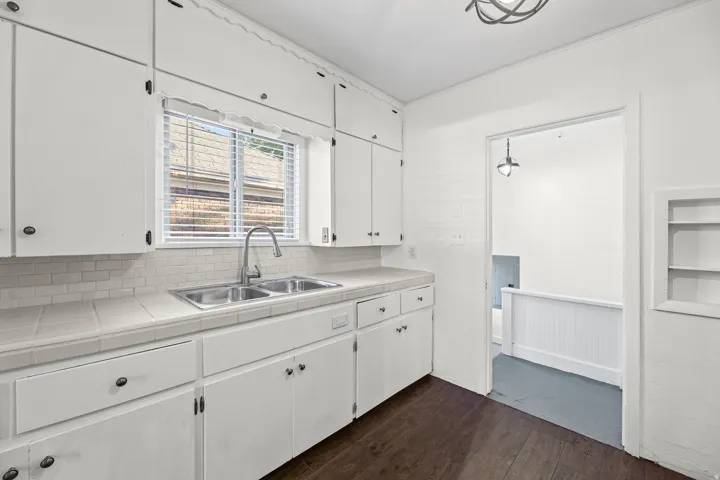 Kitchen featuring white cabinetry, tile countertops, a double basin stainless steel sink, and wood-finish flooring