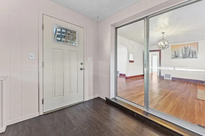Entryway featuring dark wood-finish flooring, light-toned vertical paneling, and a white door with a decorative glass insert