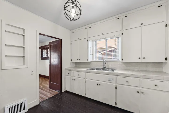 Kitchen featuring white cabinetry, a double basin stainless steel sink, subway tile backsplash, and dark wood-finish flooring