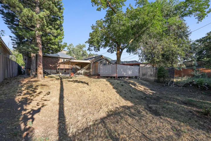 Expansive backyard featuring mature trees, a covered patio area, and a dedicated storage shed