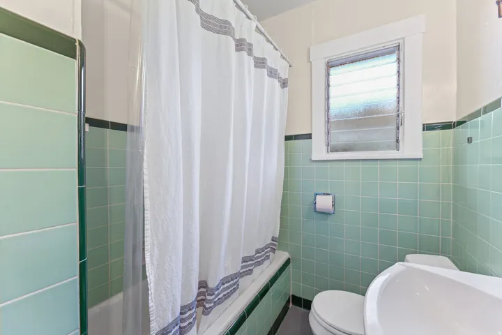 Bathroom featuring a built-in tub with green subway tile surround, white walls, and a window with frosted glass louvered panes