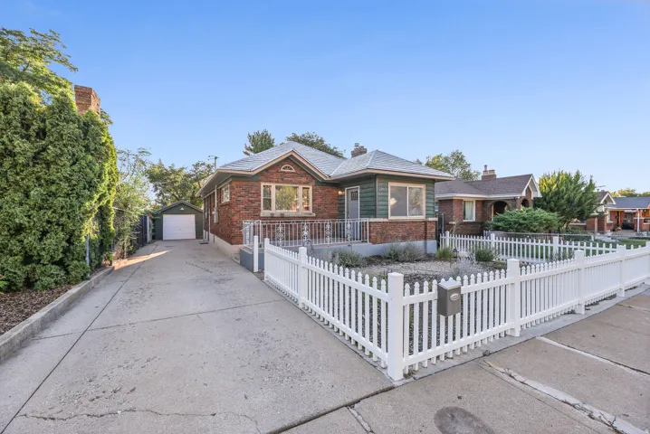 Brick and siding exterior featuring a white picket fence, concrete driveway, and detached single-car garage