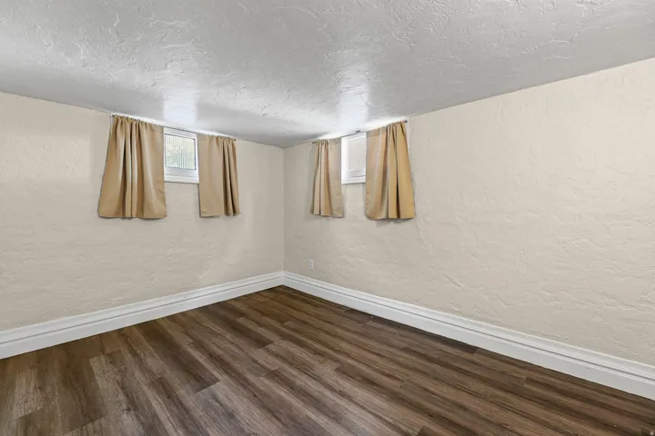 Room featuring wood-finish flooring, textured walls, and white baseboards