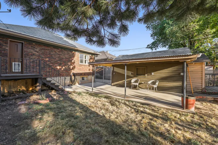 Brick exterior featuring a wooden deck with railing, concrete patio, and a covered outdoor area