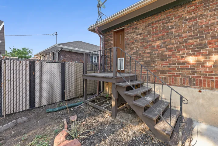 Brick exterior featuring a wooden staircase, wrought iron railings, a wooden deck, and a chain-link fence