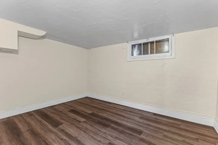 Wood-finish flooring with white baseboards, featuring a horizontal window and a wall-mounted ventilation unit