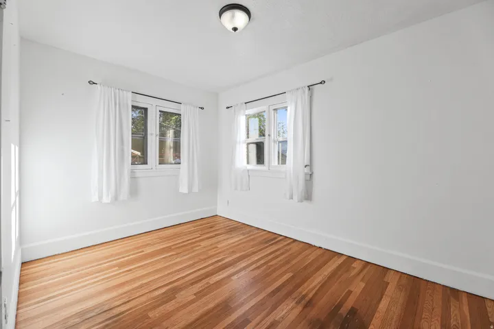 Bright room featuring wood-finish flooring, white walls, and two large windows