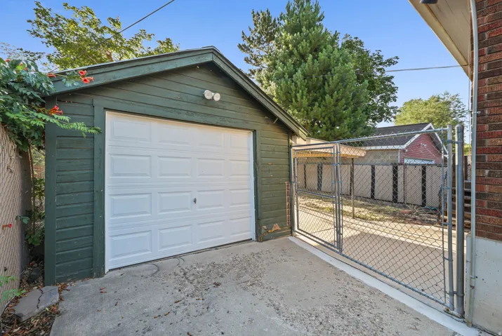 Detached garage with a paneled door, exterior wall lighting, and a sloped roof
