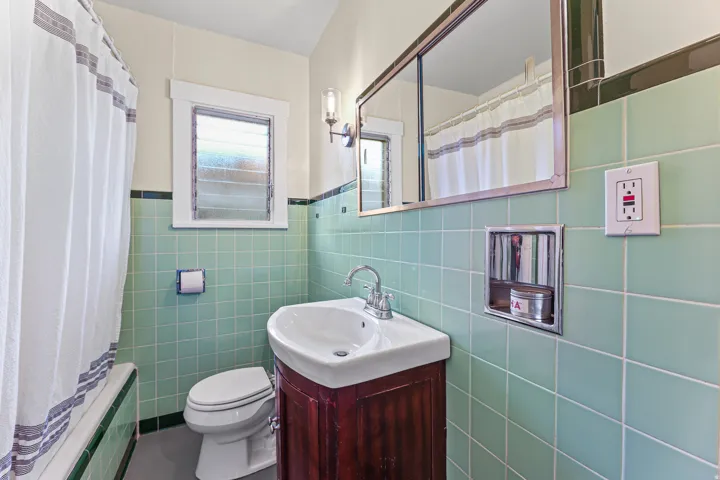 Bathroom featuring light green square tile walls with dark green trim, a wood-finish vanity with an integrated white sink, and a rectangular mirrored medicine cabinet