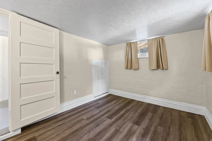 Room featuring wood-finish flooring, two windows with light-toned curtains, and a white paneled door