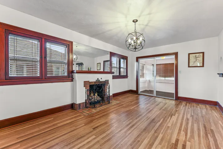 Hardwood flooring throughout, featuring a brick fireplace with an ornate screen, dark wood trim, a contemporary chandelier, and sliding glass doors