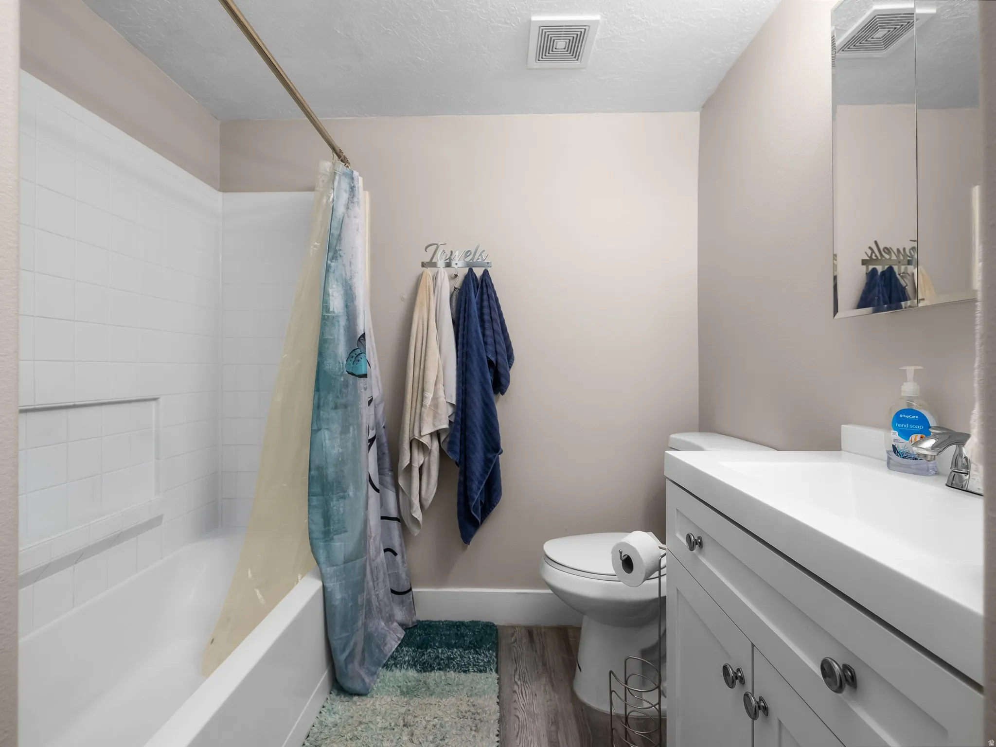 Full bathroom featuring a white tub with subway tile surround, a single vanity with storage, a wall-mounted medicine cabinet, and wood-finish flooring