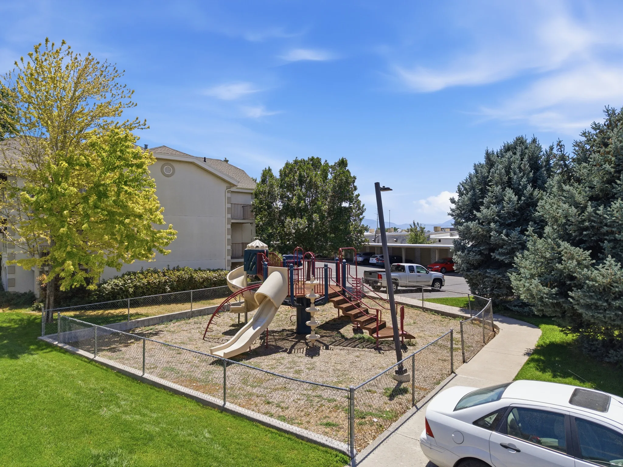 Outdoor playground structure featuring multiple slides, climbing elements, and a chain-link fence enclosure