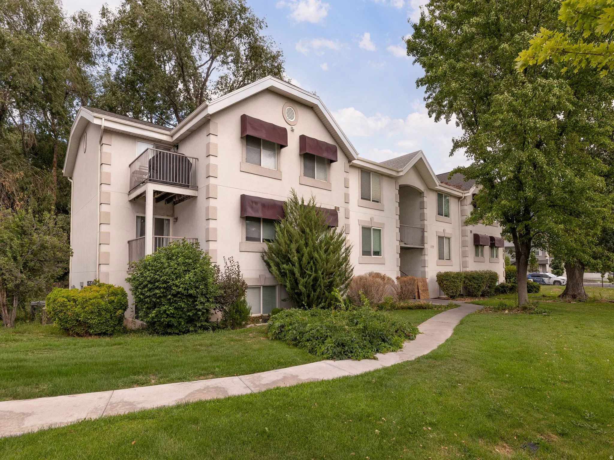 Multi-story building featuring light-colored stucco exterior with stone-look corner accents, multiple private balconies, and shaded windows with dark awnings