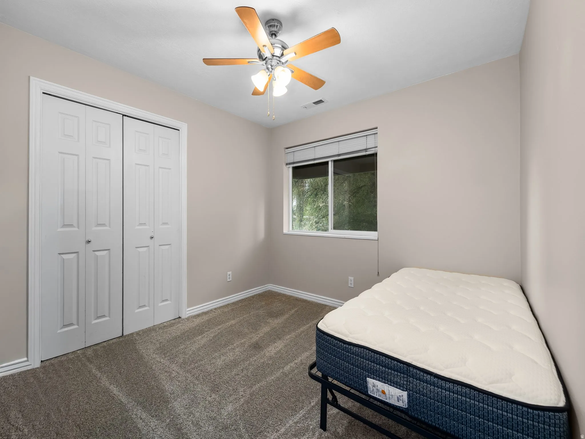 Carpeted room featuring a ceiling fan with light fixture, window with blinds, and white bi-fold closet doors