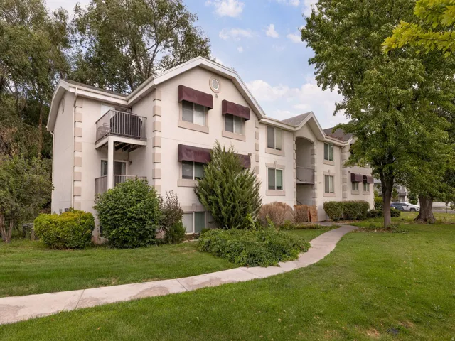 Multi-story building featuring light-colored stucco exterior with stone-look corner accents, multiple private balconies, and shaded windows with dark awnings