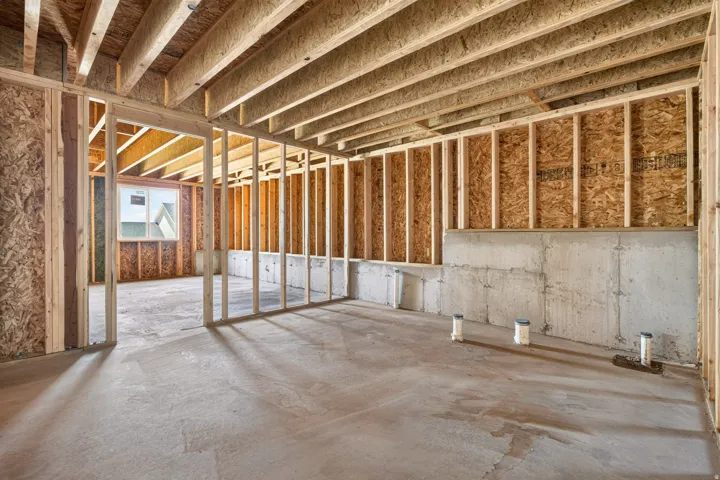 Unfinished lower level featuring concrete slab flooring, wood framing, a concrete foundation wall, and visible plumbing stub-outs
