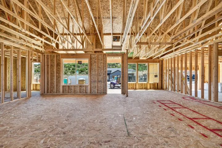 Open-concept framing showcasing structural wood beams, exposed trusses, multiple windows, and oriented strand board flooring