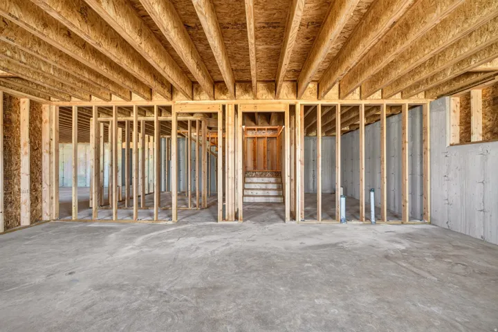 Unfinished basement featuring concrete flooring, wood framing, exposed joists, and a partial staircase