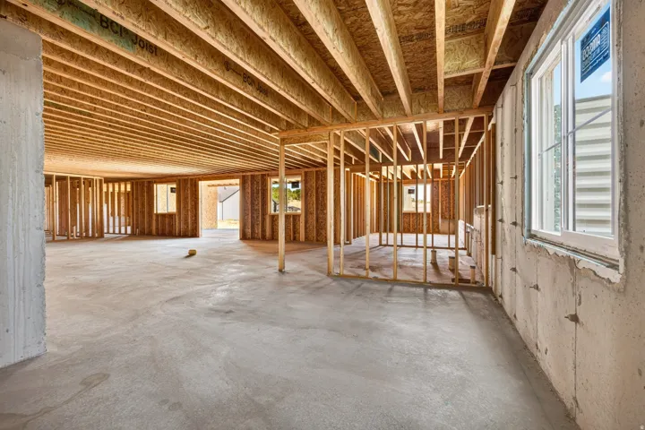 Unfinished basement space featuring exposed wood framing, concrete flooring, and multiple windows