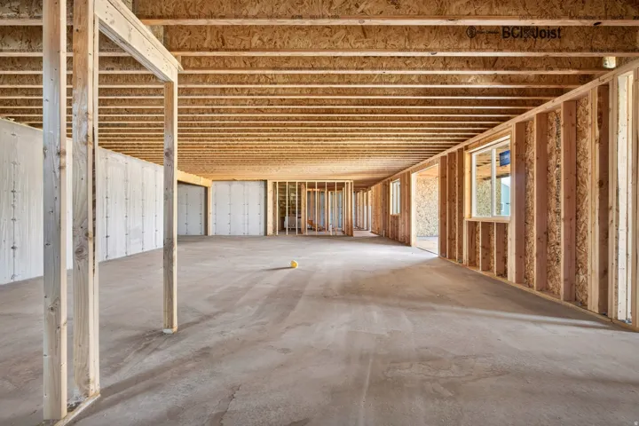Unfinished lower level featuring concrete slab flooring, exposed wood framing, and multiple window openings