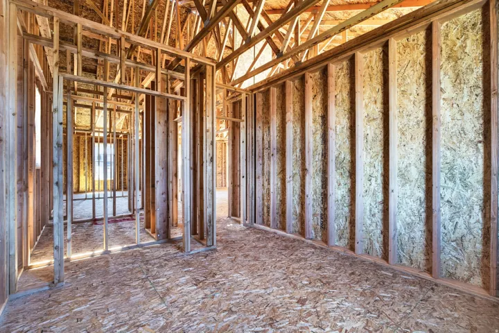 Interior framing of a new construction home featuring exposed wood studs, oriented strand board (OSB) wall sheathing, and OSB subflooring