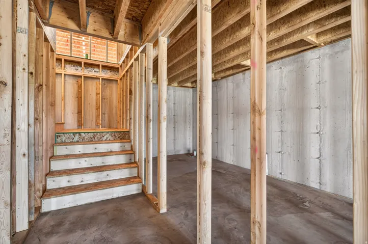 Unfinished basement area featuring a concrete foundation, exposed wood framing, and wood stairs leading to an upper level