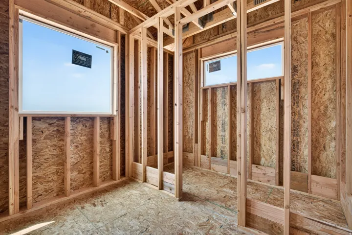 New construction framing showcasing wooden studs, oriented strand board sheathing, and two installed windows providing natural light