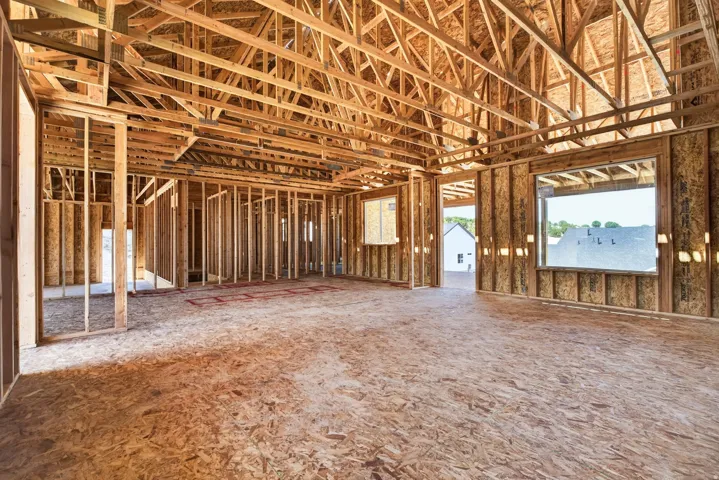 New construction framing featuring engineered wood flooring, substantial window openings, and visible ceiling trusses