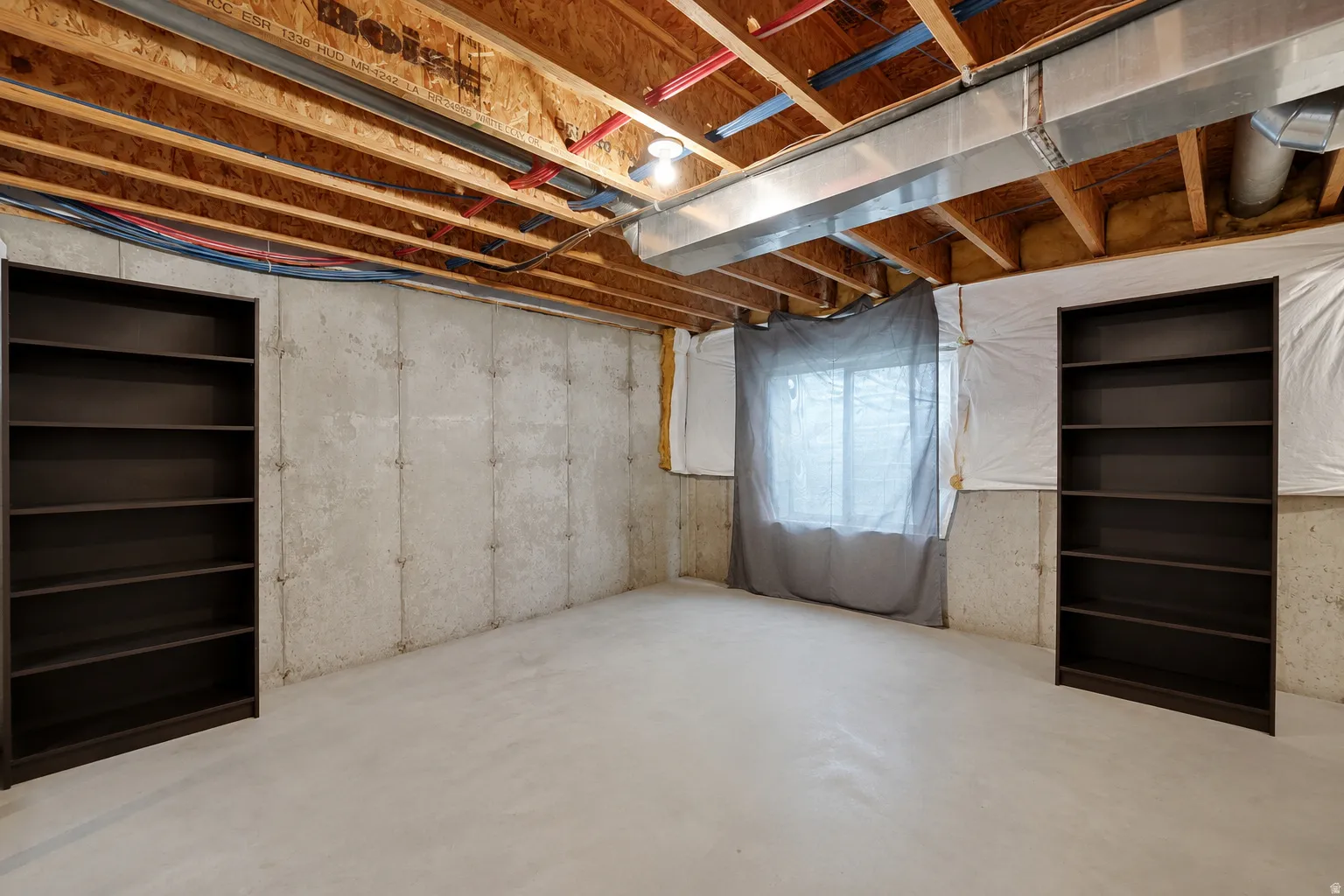 Unfinished lower level featuring exposed ceiling joists, poured concrete walls, and a window opening
