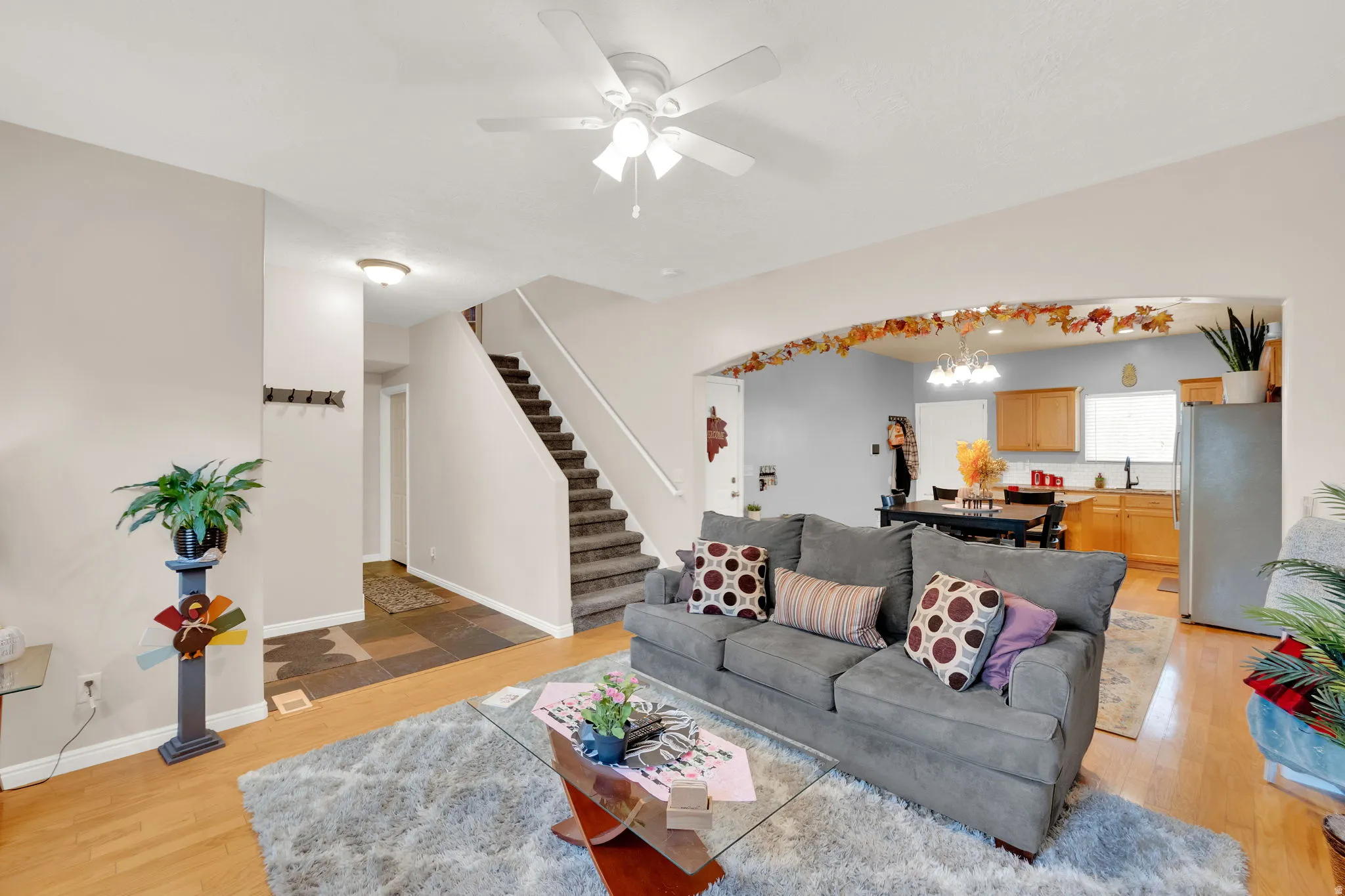 Open-concept living space featuring wood-finish flooring, a ceiling fan with integrated lighting, and an arched entryway leading to the kitchen area