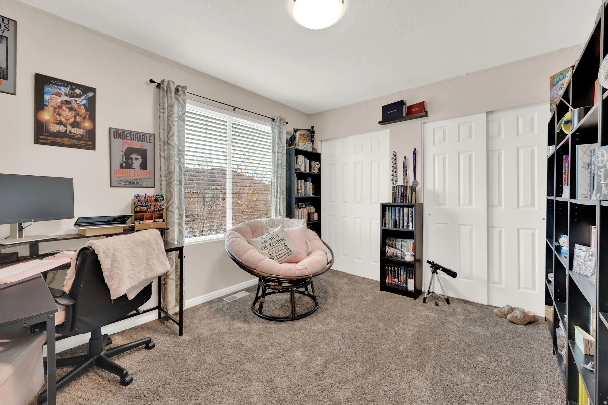 Spacious room featuring neutral carpeting, a large window with horizontal blinds, and two sets of bi-fold closet doors