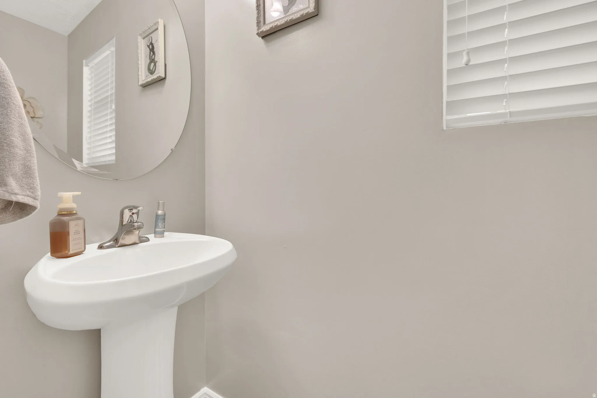 White pedestal sink with a chrome faucet, illuminated by natural light from a window with white blinds
