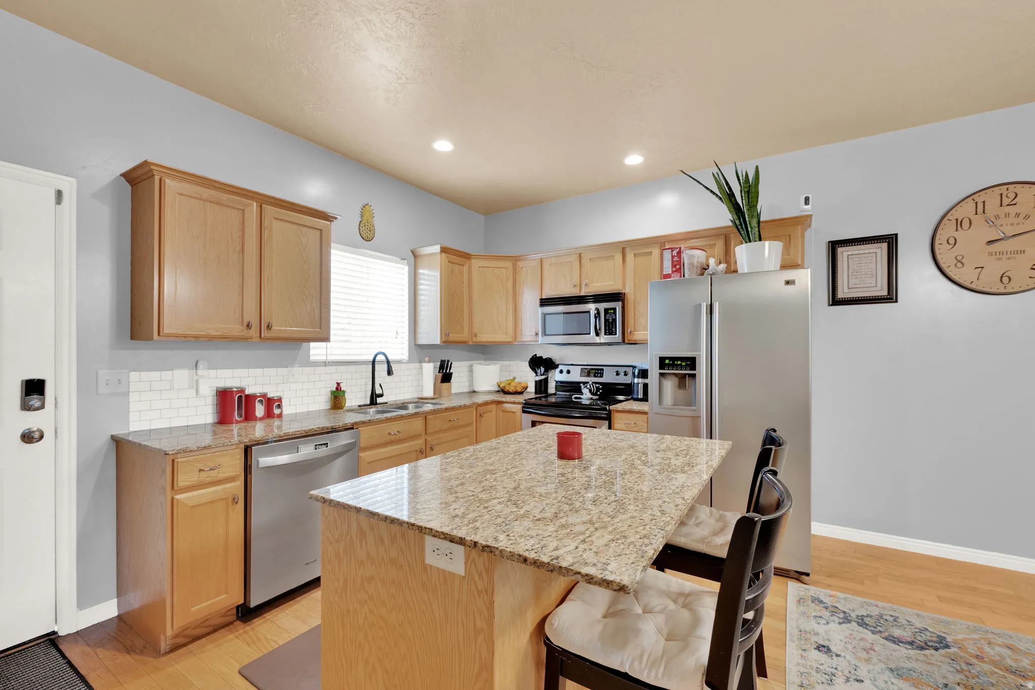 Kitchen featuring a central island with granite countertop, light wood cabinetry, stainless steel appliances, and a white subway tile backsplash
