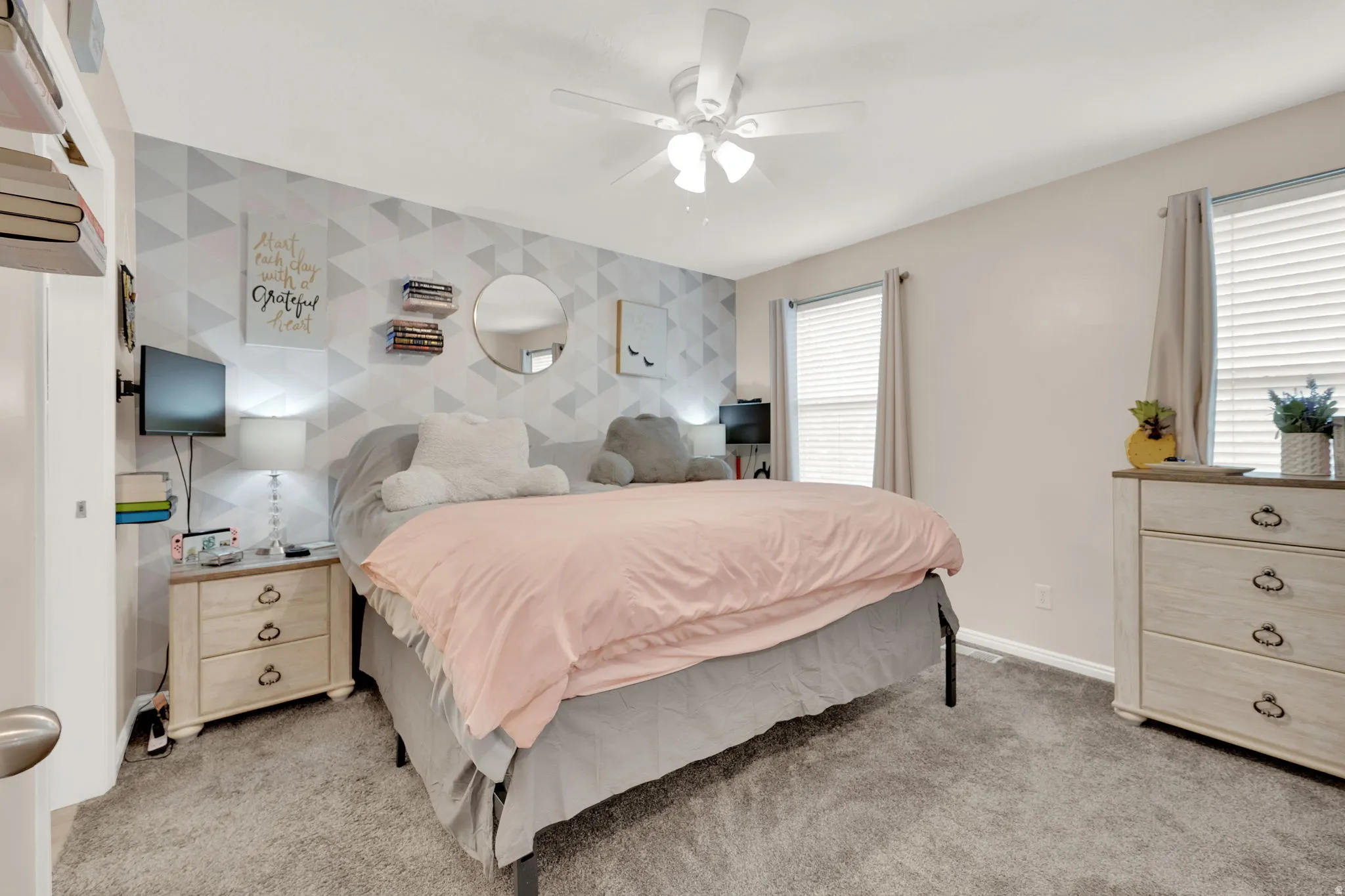 Spacious room featuring neutral carpeting, a geometrically patterned accent wall, and a ceiling fan with integrated lighting