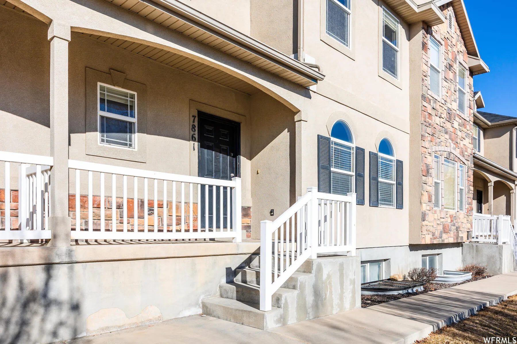 Stucco exterior with stone accents and a covered front porch featuring white railings