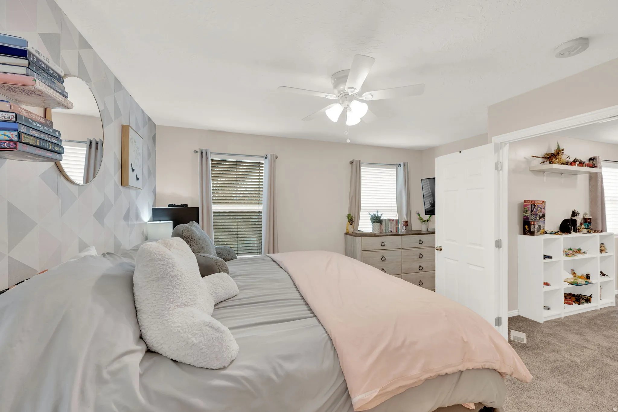 Carpeted bedroom featuring a geometric accent wall, multiple windows with blinds, and a ceiling fan with integrated lighting