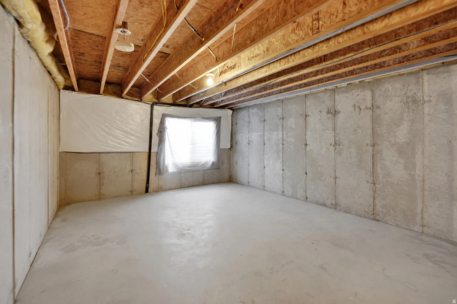 Unfinished basement offering exposed wood ceiling joists, concrete flooring, concrete foundation walls, and a window opening