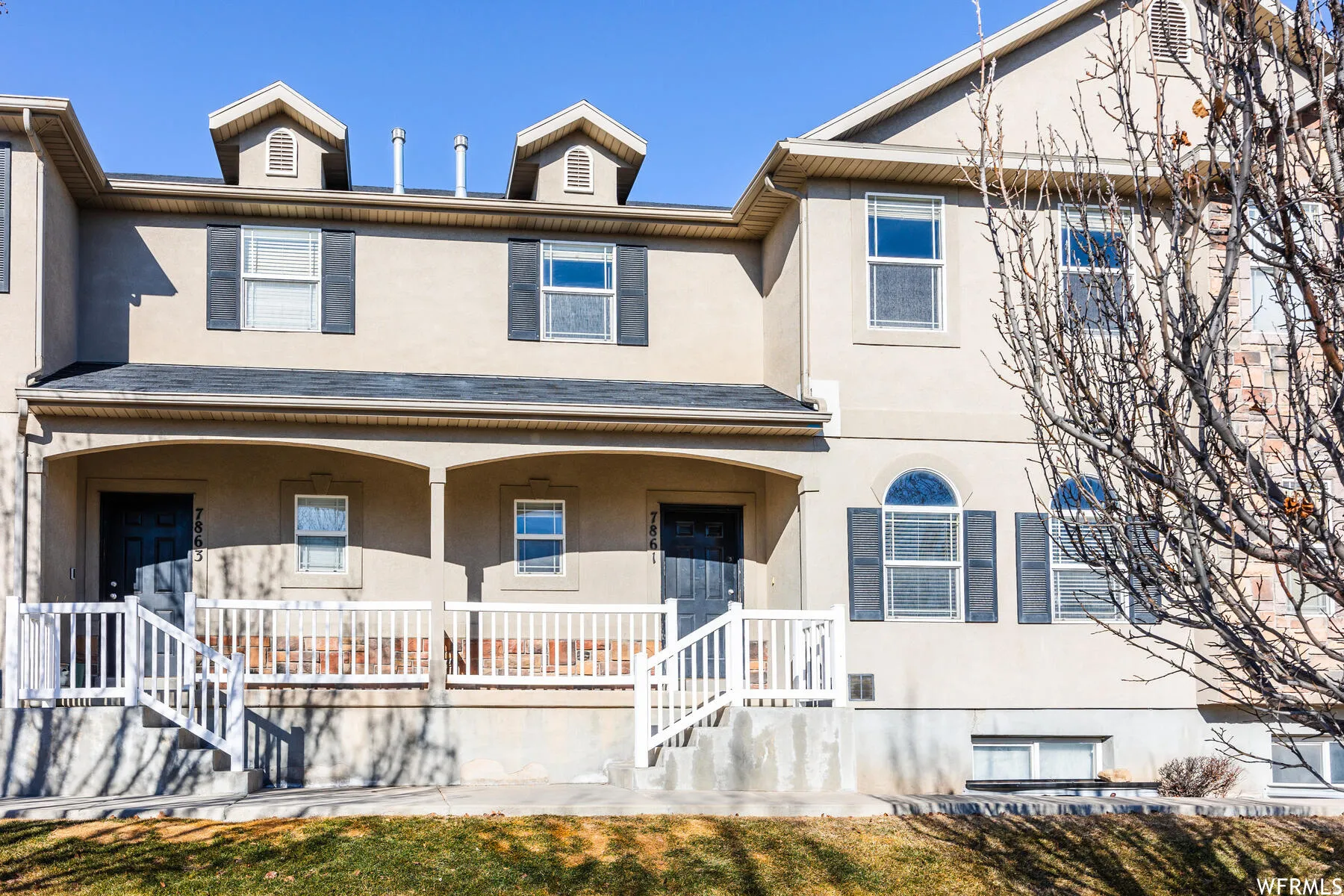 Two-story townhome exterior featuring an arched entryway, dormer windows, and a covered porch with white railings
