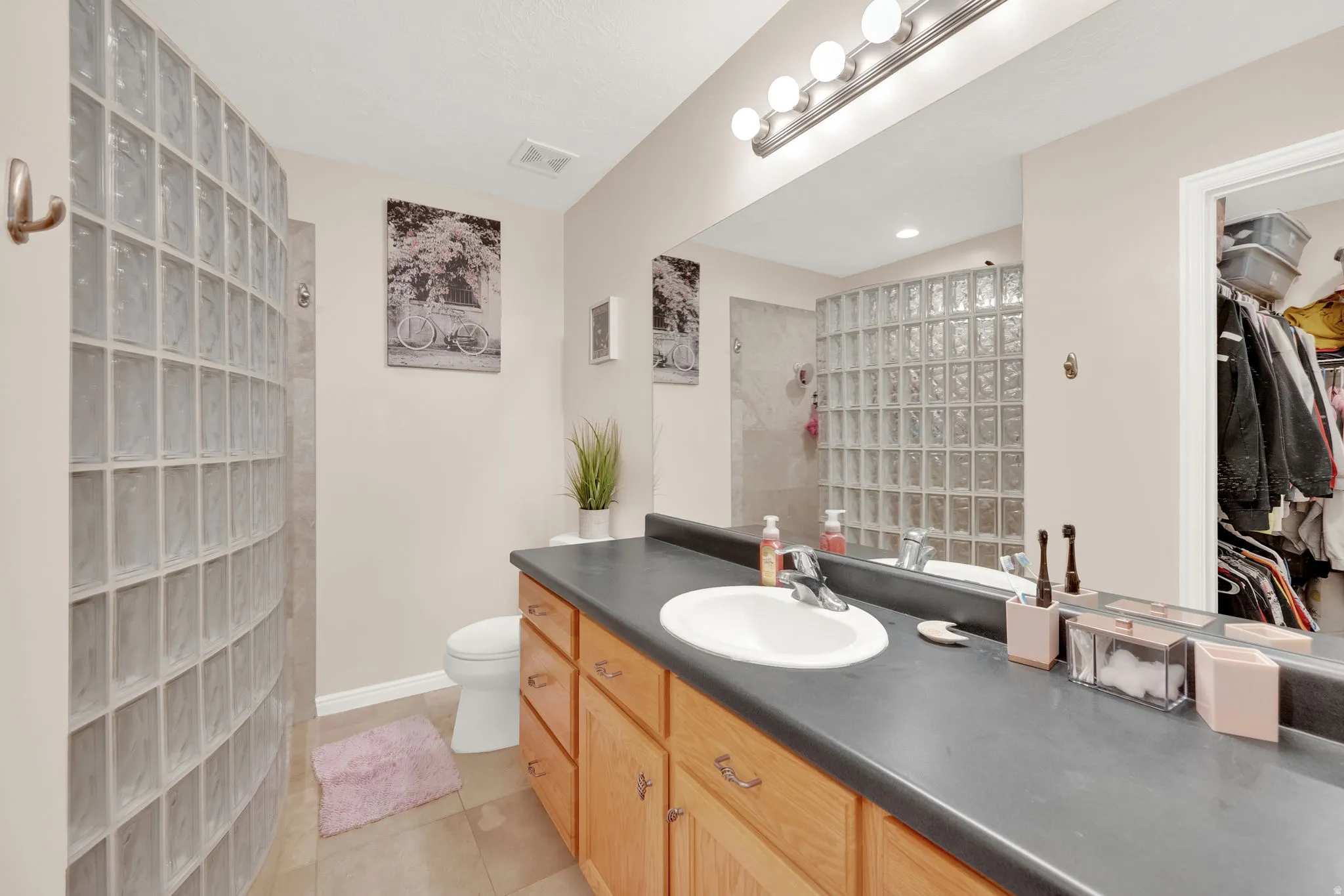 Bathroom featuring a curved glass block shower enclosure, a single vanity with wood cabinetry, a dark countertop, and tile flooring