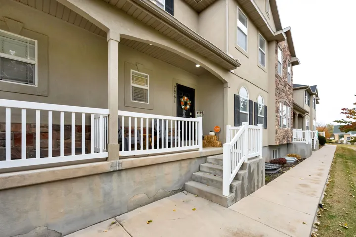 Townhome exterior featuring a stucco facade, stone accents, white railing, covered porch, and concrete walkway