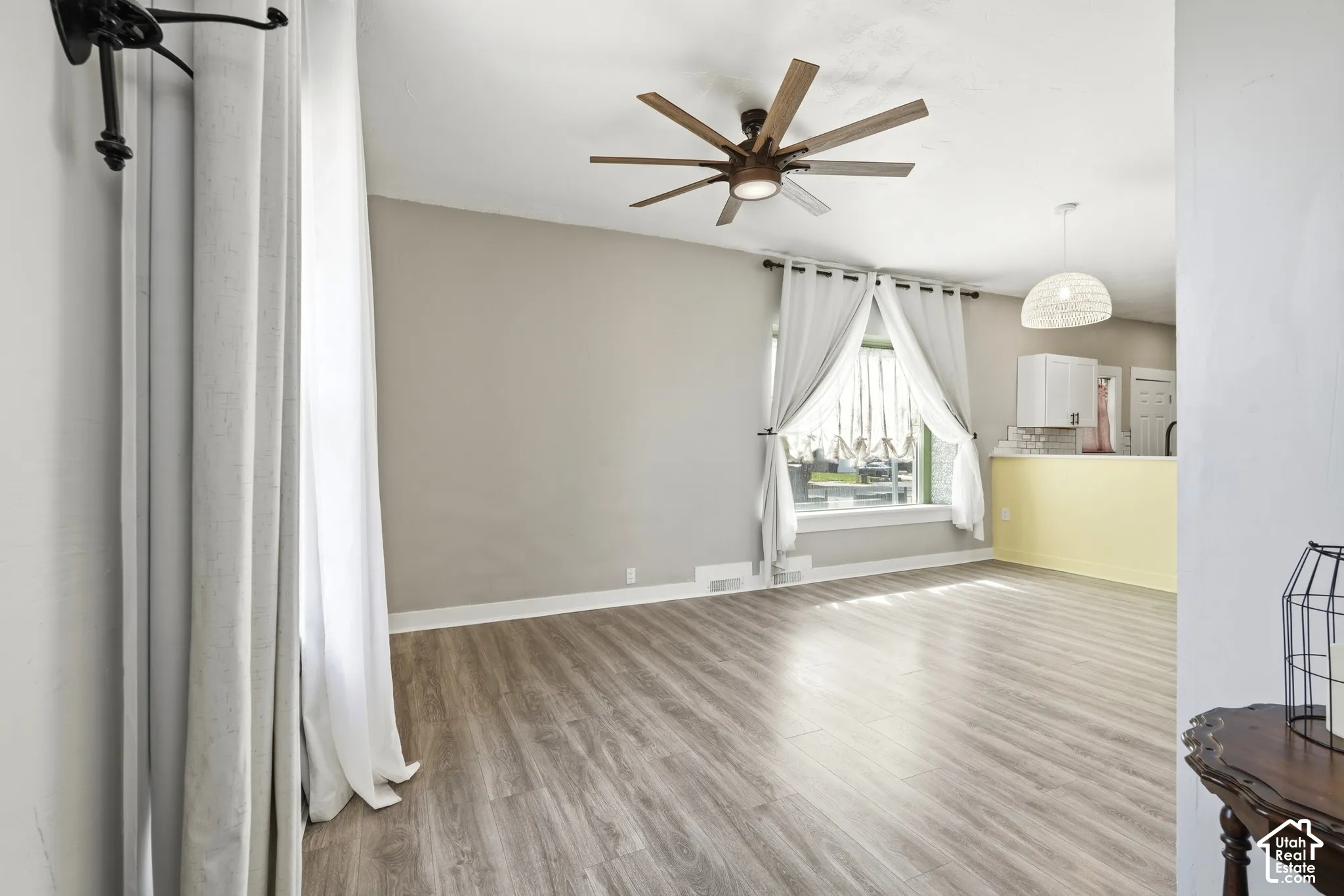 Spacious room featuring wood-finish flooring, a contemporary ceiling fan with multiple blades, and light-colored walls