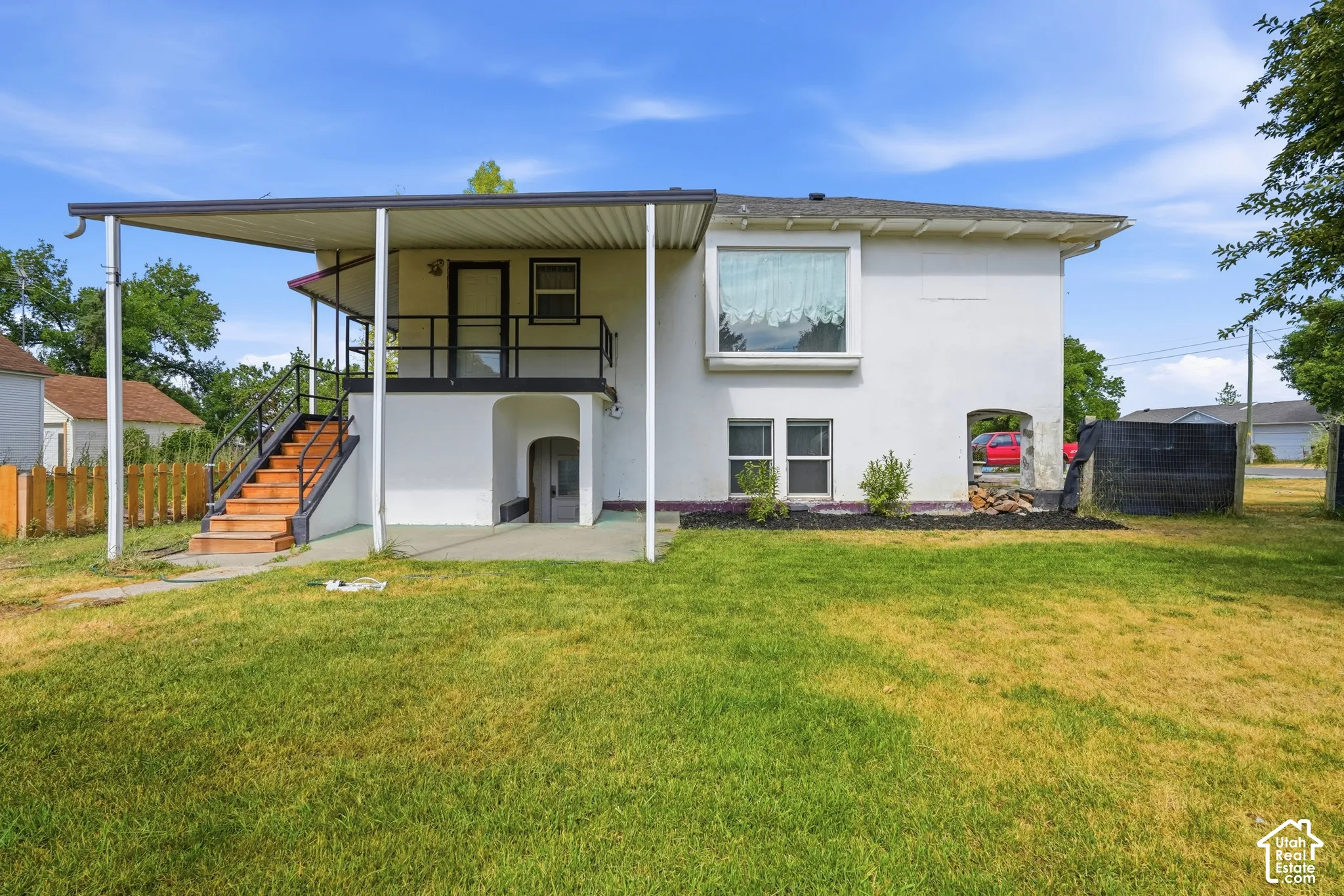 Rear exterior featuring a covered porch, external staircase with black railings, and a ground-level arched entry