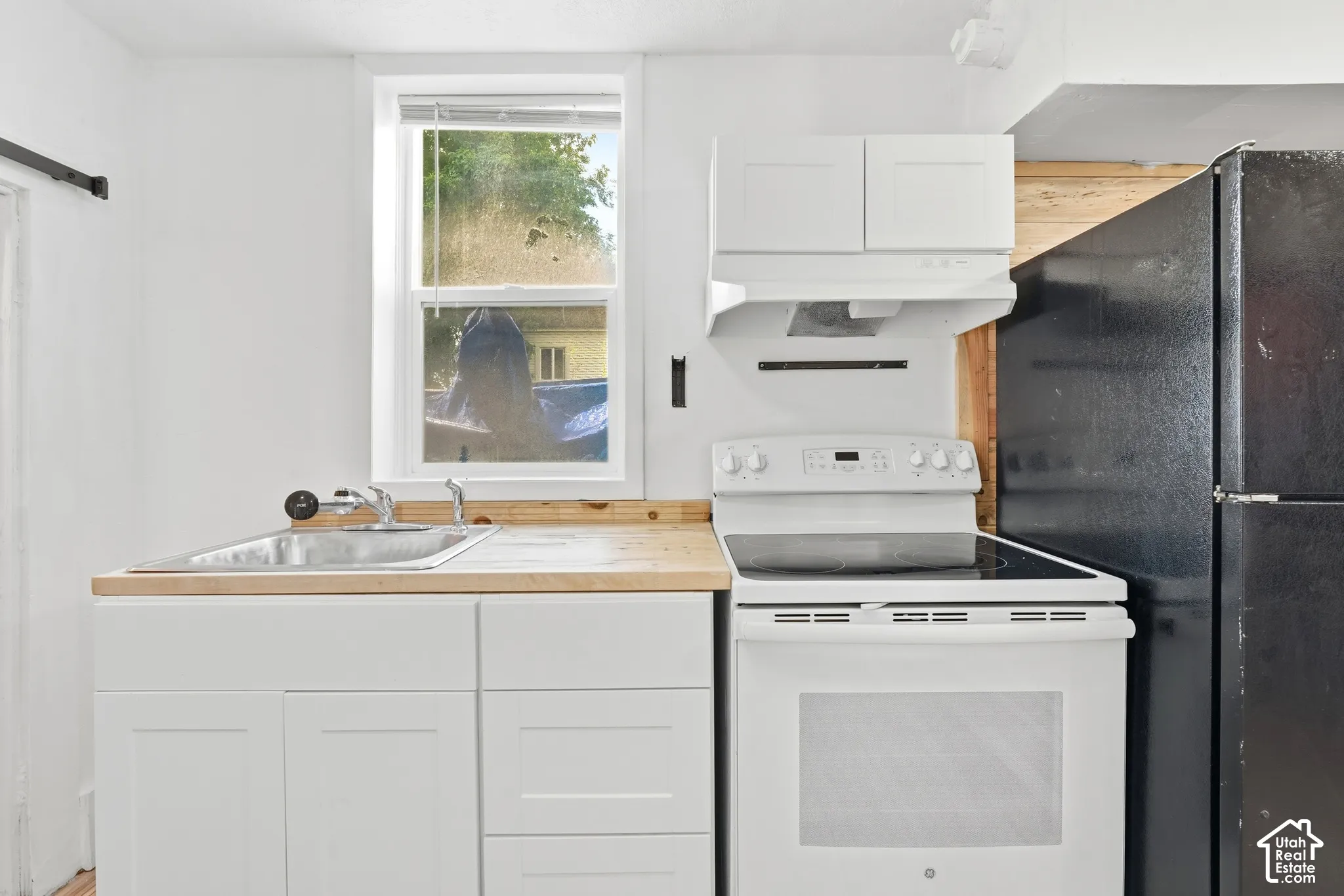 Kitchen featuring light wood-finish countertops, white cabinetry, a stainless steel sink, a white electric range, and an overhead microwave hood