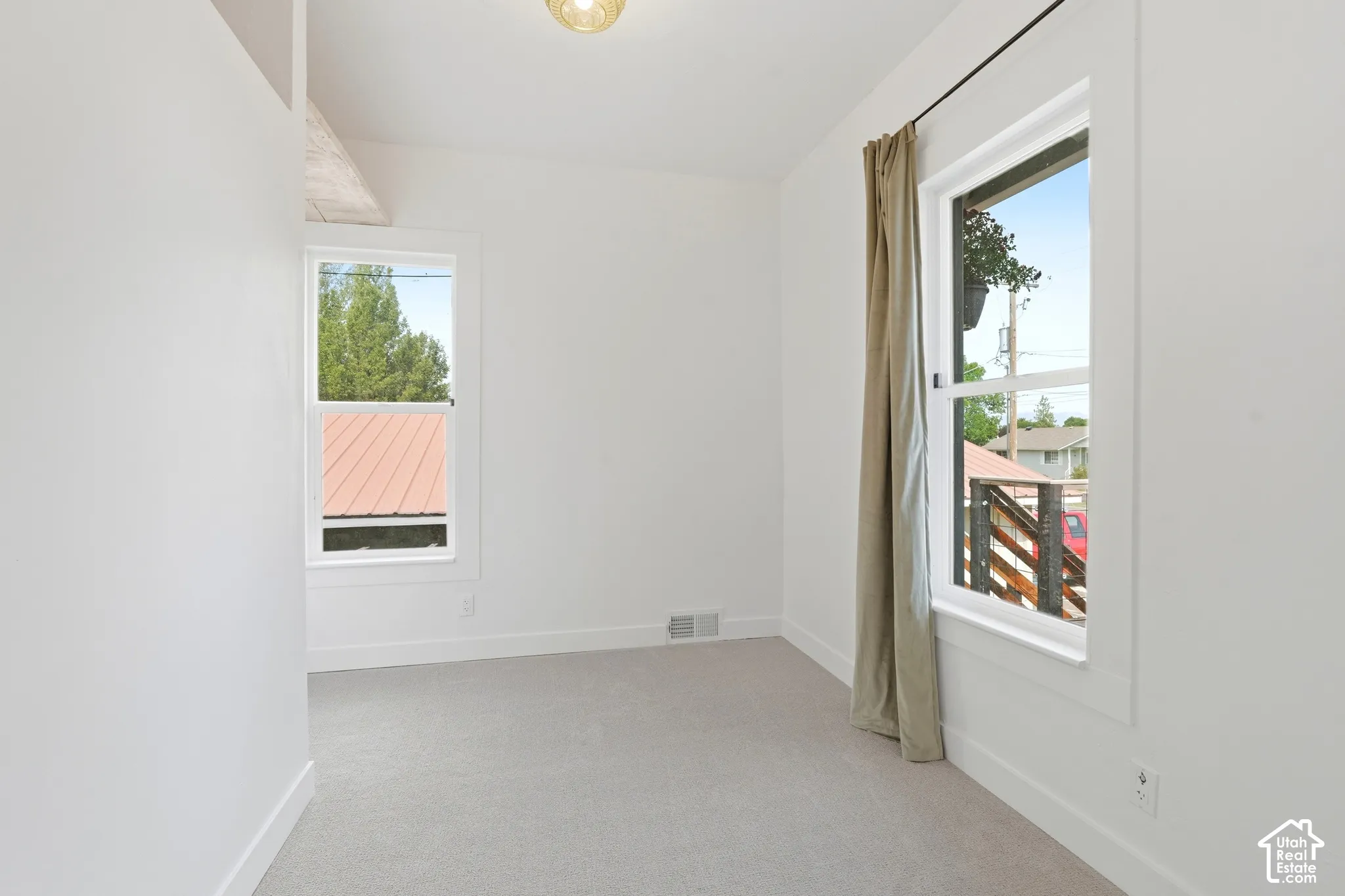 Bright interior space featuring two windows with white trim, light-toned carpeting, white walls, and a ceiling-mounted light fixture