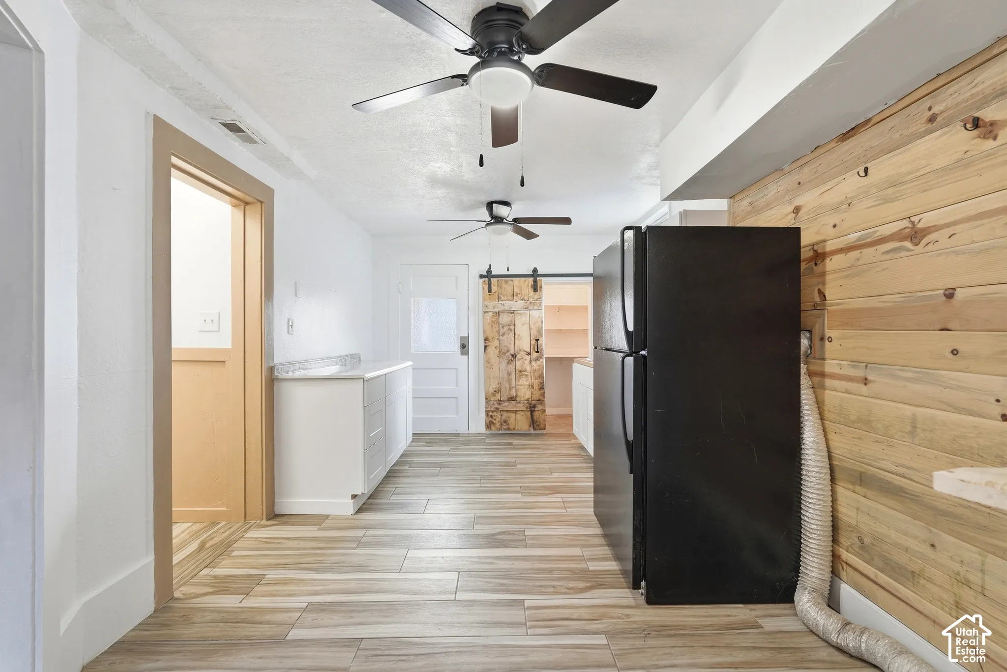 Interior space featuring wood-finish flooring, white cabinetry with a light-toned countertop, and multiple ceiling fans