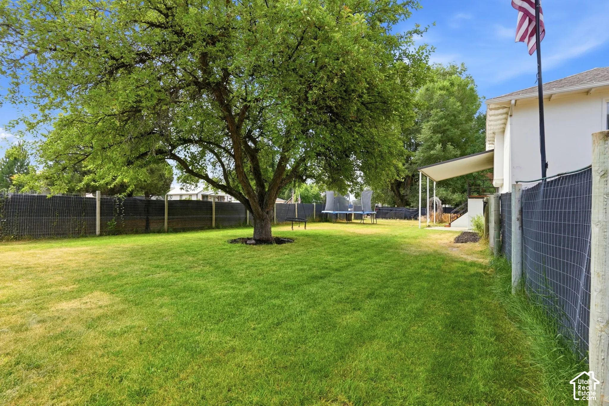 Spacious backyard featuring a large shade tree, expansive lawn, white-painted exterior, covered patio area, and wire fencing