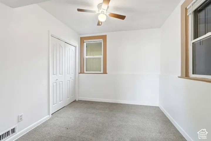 Carpeted room featuring a ceiling fan, two windows with wood-finish trim, white paneled walls, and a bi-fold closet door