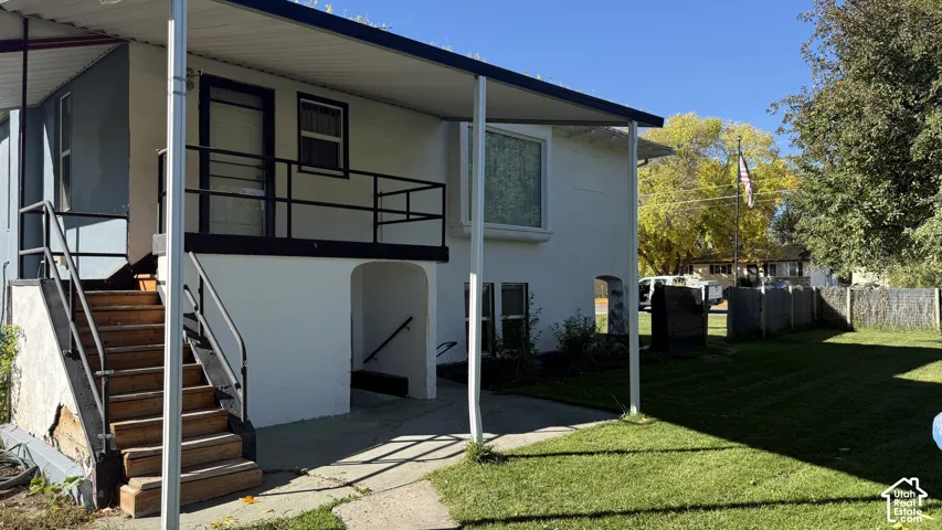 Exterior featuring a covered porch, metal staircase with railing, smooth stucco finish, picture window, and a spacious lawn